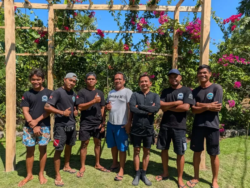 Groupe de six personnes souriantes, bras croisés, devant un jardin fleuri