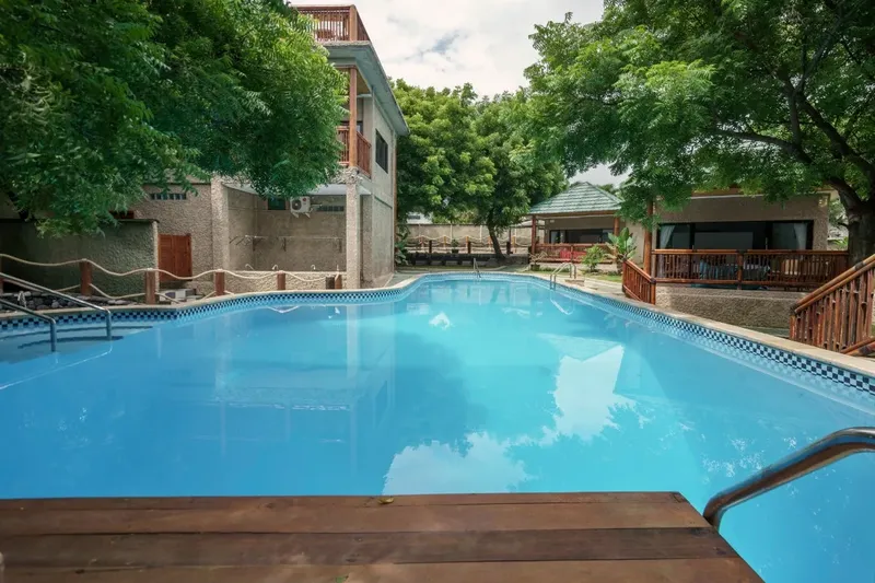 Piscine bleue devant un bâtiment et végétation luxuriante ensoleillée
