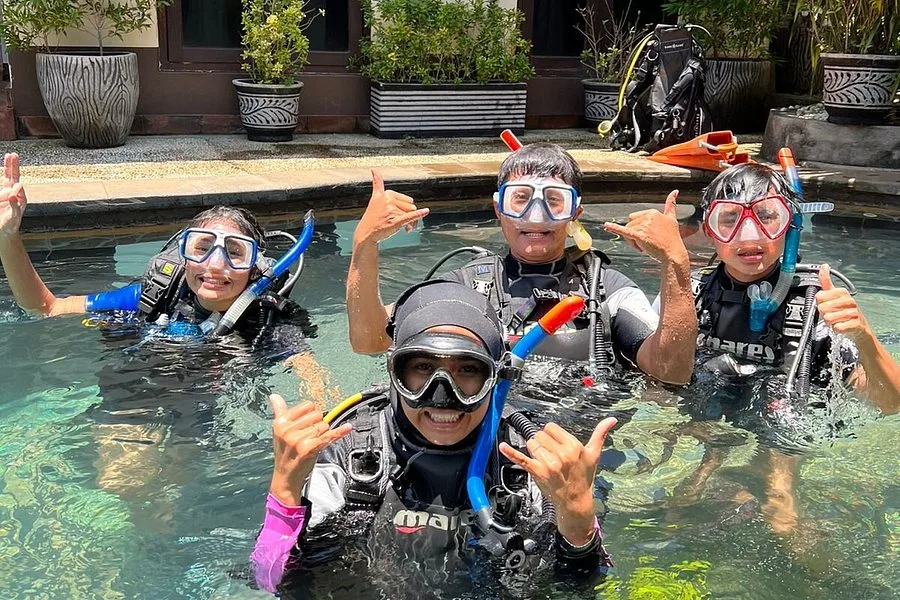 Quatre plongeurs souriants font le signe shaka dans une piscine