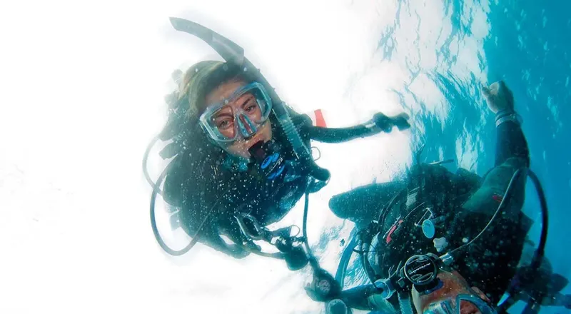 Deux plongeurs souriants avec équipement complet dans l'eau bleue