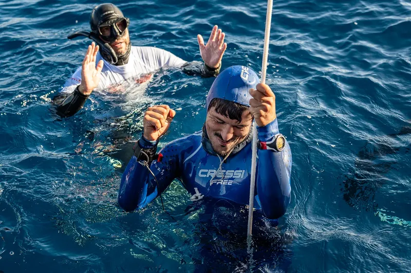 Deux apnéistes en combinaison s'aident mutuellement dans l'eau bleue