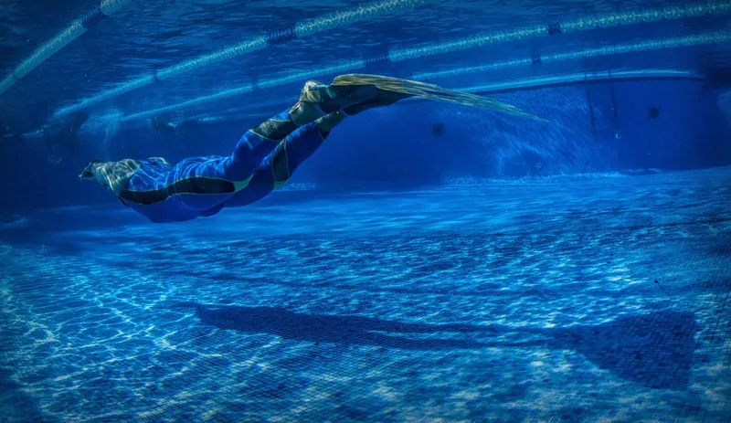 Apnéiste en combinaison nageant sous l'eau dans une piscine bleue