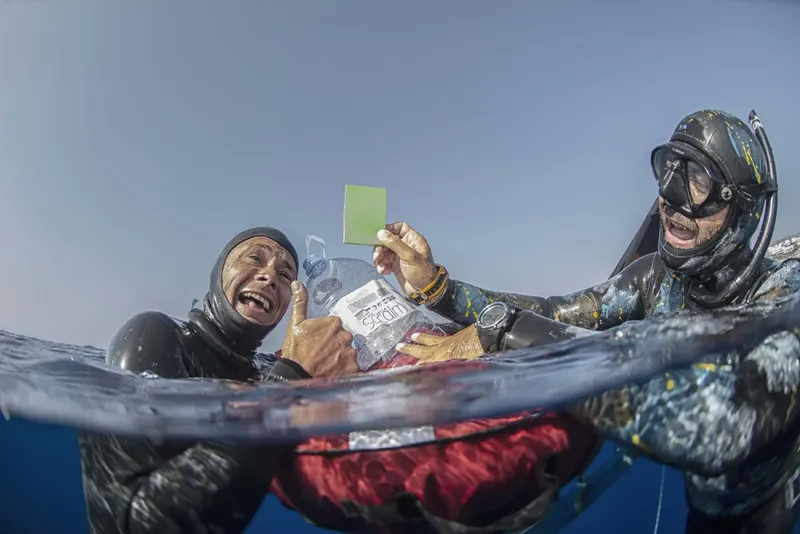 Deux apnéistes sourient et montrent une carte de score en mer