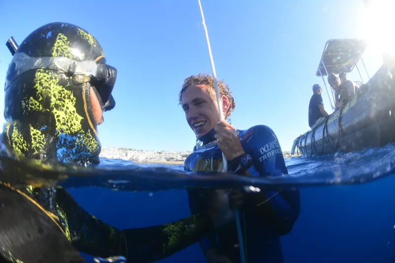 Deux plongeurs en apnée sourient, un bateau est à l'arrière-plan