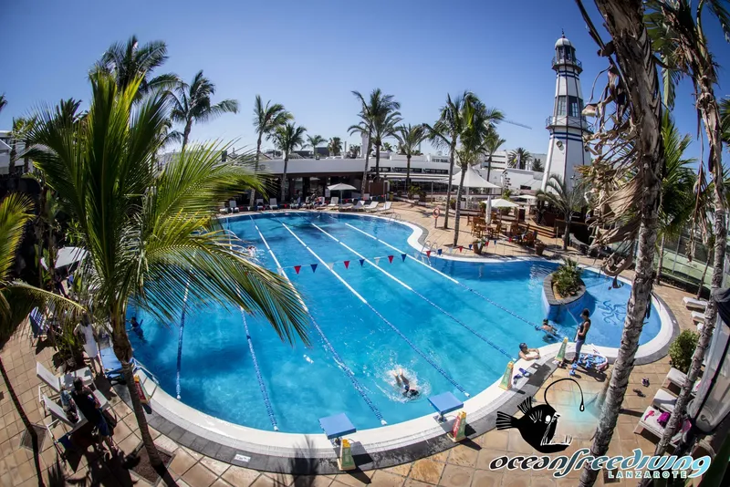 Vue aérienne d'une piscine avec des nageurs et un phare en arrière-plan