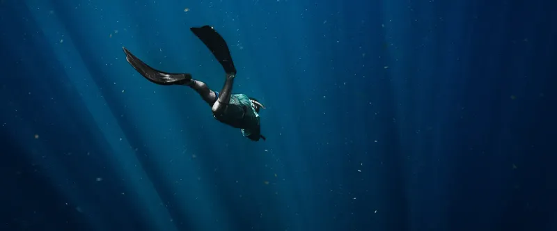 Apnéiste en plongée libre, corps en extension dans l'eau bleue