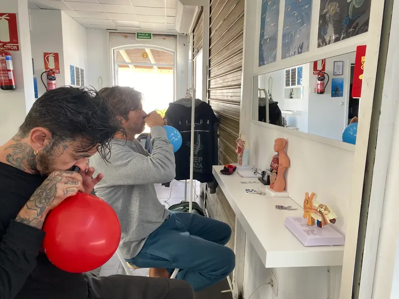 Deux personnes dans un intérieur, un homme gonfle un ballon bleu