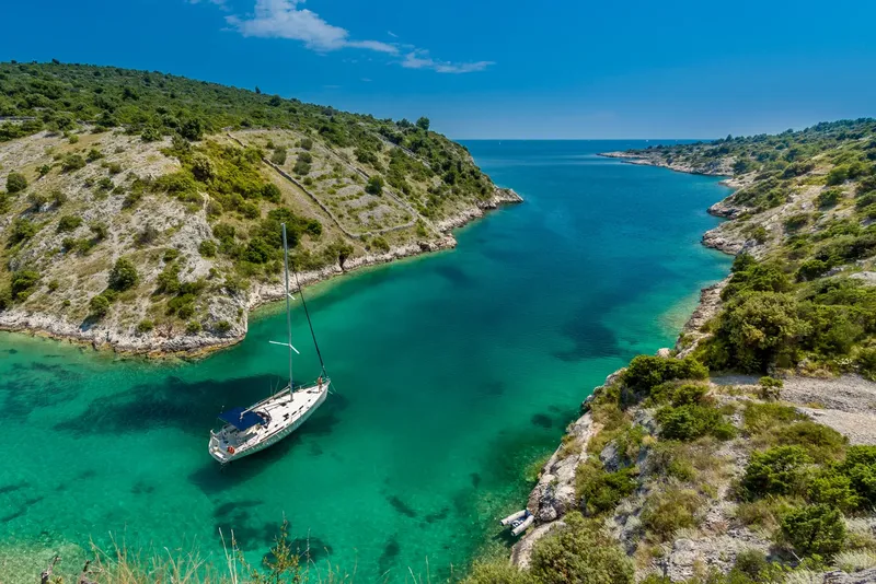 Voilier amarré dans une crique turquoise entourée de collines verdoyantes