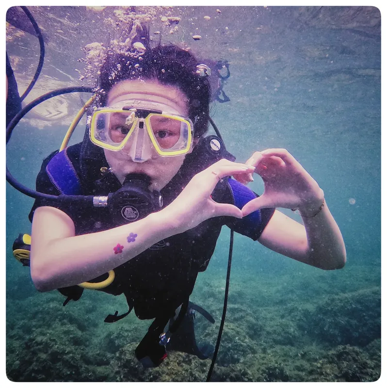 Plongeuse souriante forme un cœur avec ses mains sous l'eau