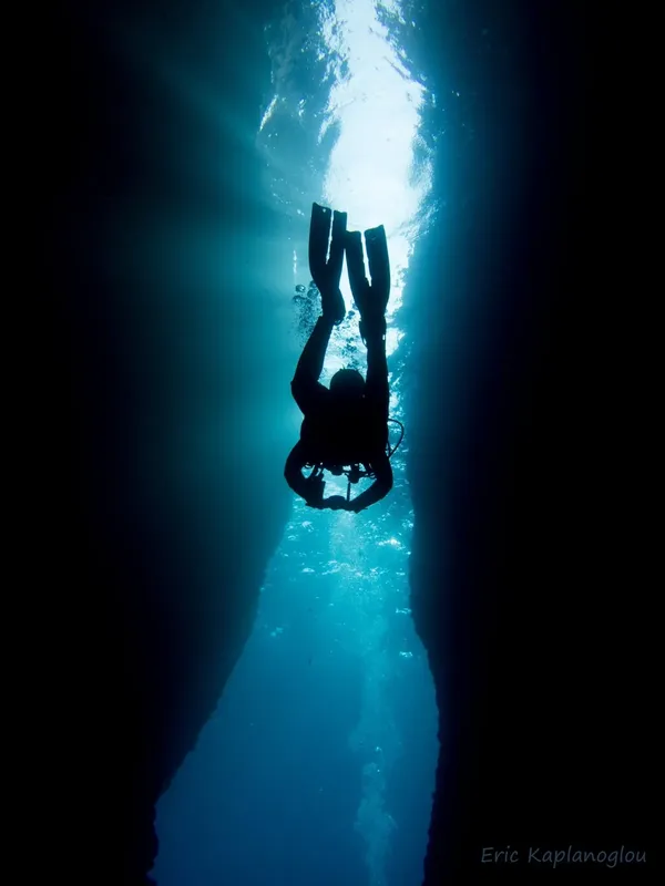 Plongeur silhouette sombre explorant une faille sous-marine éclairée par le soleil