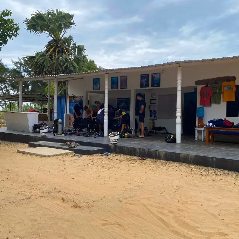 Plage avec bâtiment, personnes équipées pour la plongée et matériel