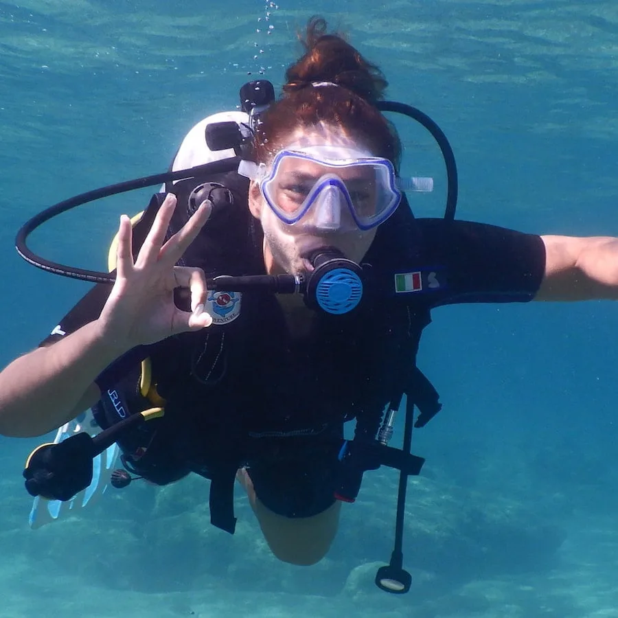 Plongeuse souriante avec équipement complet, nageant dans une eau turquoise claire