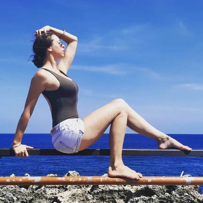 Jeune femme assise sur une rambarde, regardant vers l'horizon marin