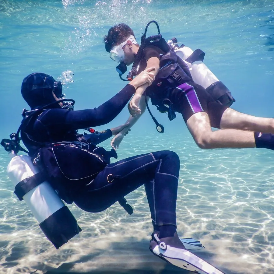 Deux plongeurs s'entraident sous l'eau avec leur équipement complet