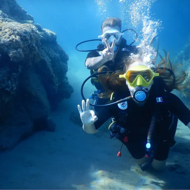 Deux plongeurs souriants font des signes de la main sous l'eau