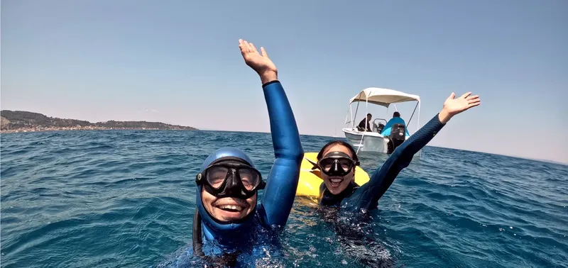 Deux plongeurs en combinaison sourient et lèvent les bras dans l'eau