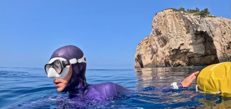Plongeur en combinaison nageant en mer face à une falaise rocheuse