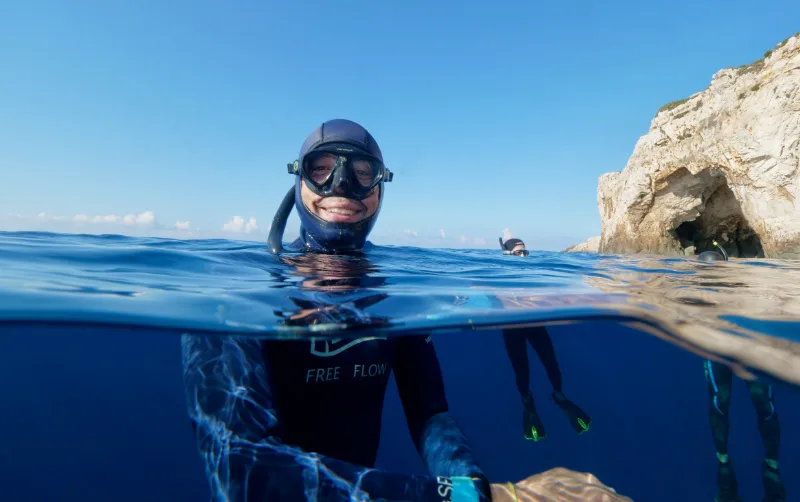 Apnée : plongeur souriant à la surface, vue moitié aérienne moitié sous-marine