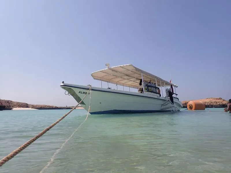 Bateau de plongée blanc avec auvent, amarré dans une eau turquoise claire