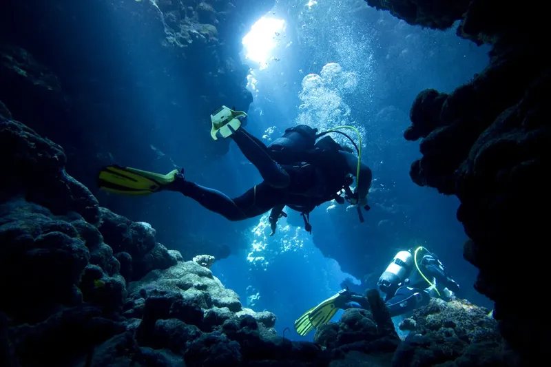 Deux plongeurs explorent une grotte sous-marine avec des rayons de lumière