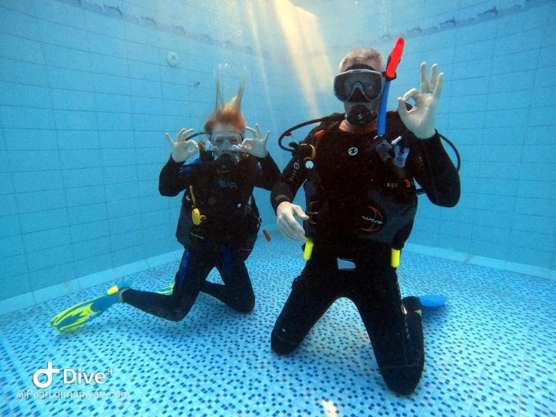 Deux plongeurs souriants font des signes OK dans une piscine
