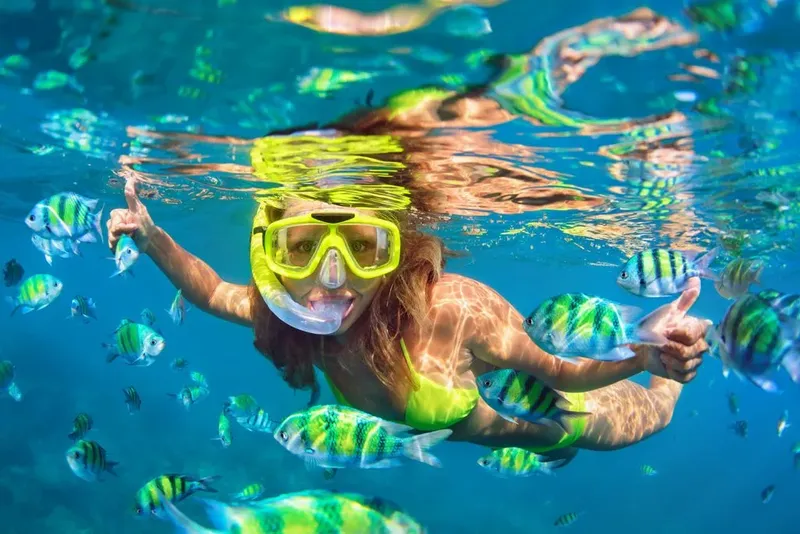 Plongeuse souriante entourée de nombreux poissons tropicaux colorés
