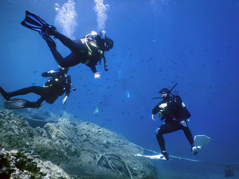 Trois plongeurs explorent un récif rocheux dans une eau bleue claire