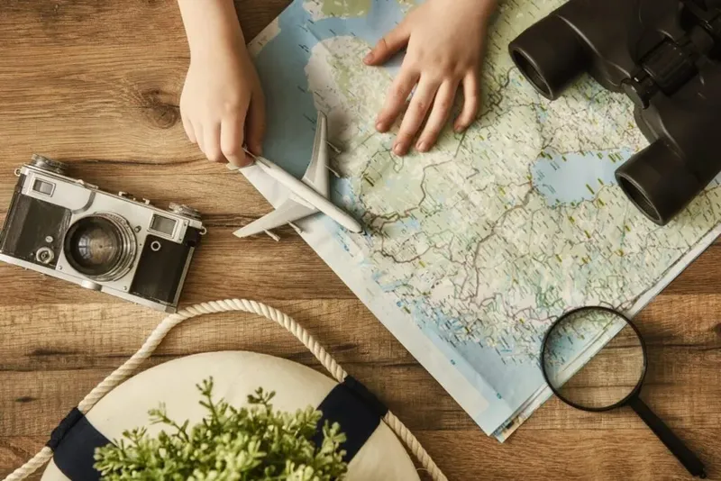 Mains tenant un avion sur une carte, jumelles et loupe