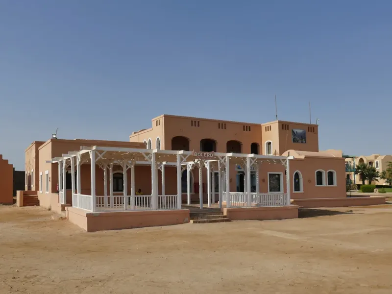 Bâtiment beige avec pergola, devant un paysage désertique ensoleillé