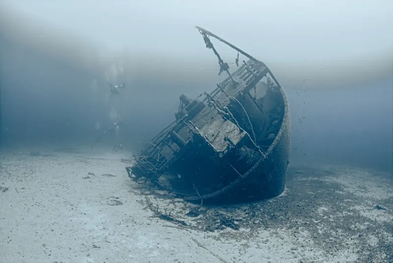 Epave de bateau coulee sur fond sableux avec un plongeur