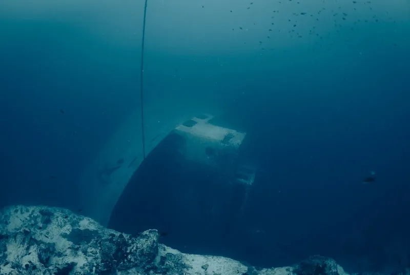 Epave sombre sous l'eau, roche au premier plan, lumière bleutée