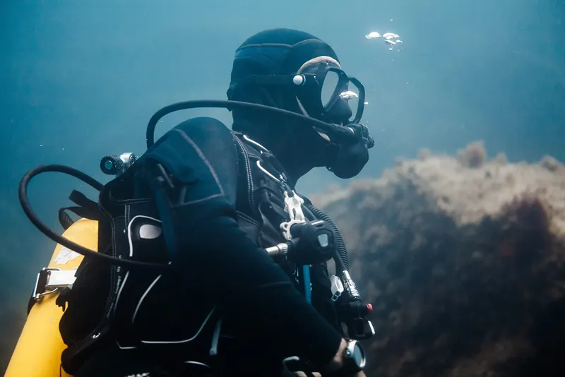 Plongeur en combinaison noire explore les fonds marins bleus et rocheux