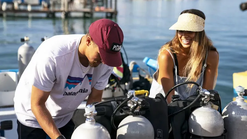 Deux personnes souriantes préparent du matériel de plongée sur un bateau