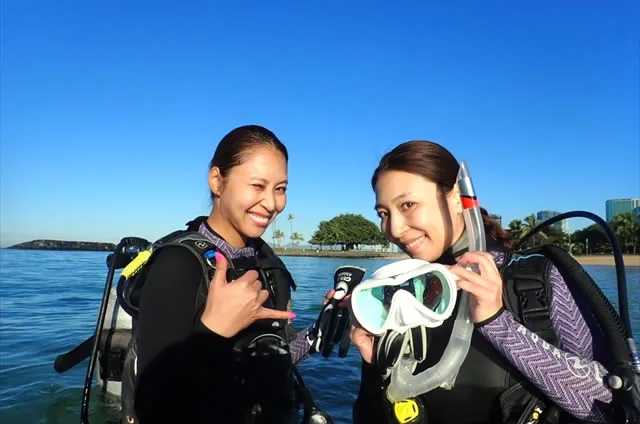 Deux plongeuses souriantes avec leur équipement sur une plage ensoleillée