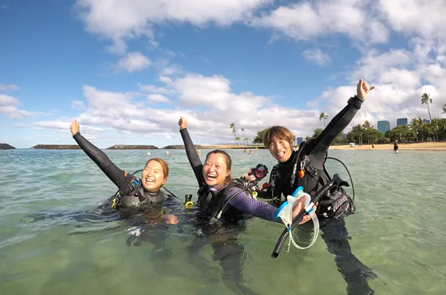 Trois plongeuses souriantes sortent de l'eau avec leur équipement