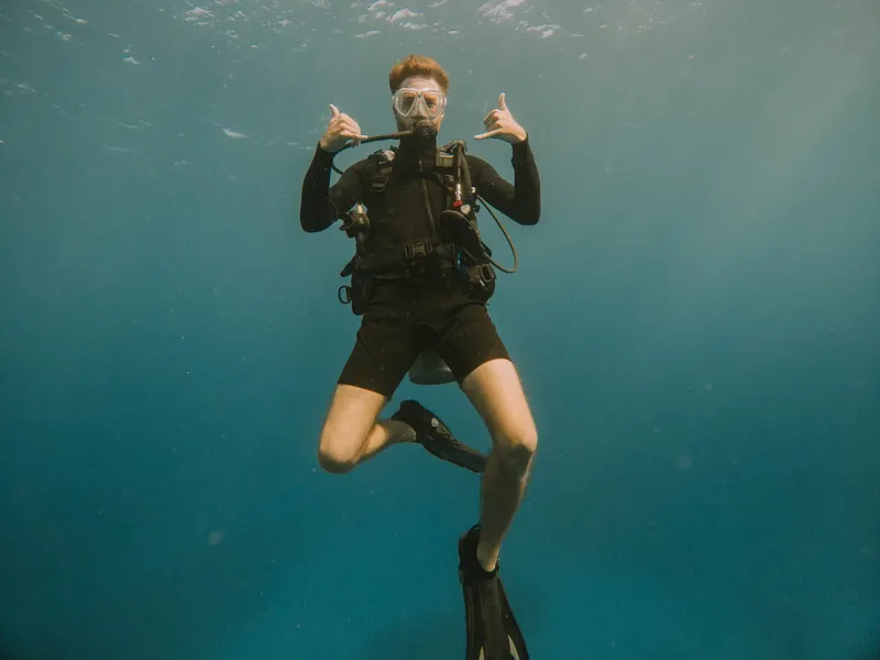 Plongeur souriant avec signe de la main sous l'eau bleue