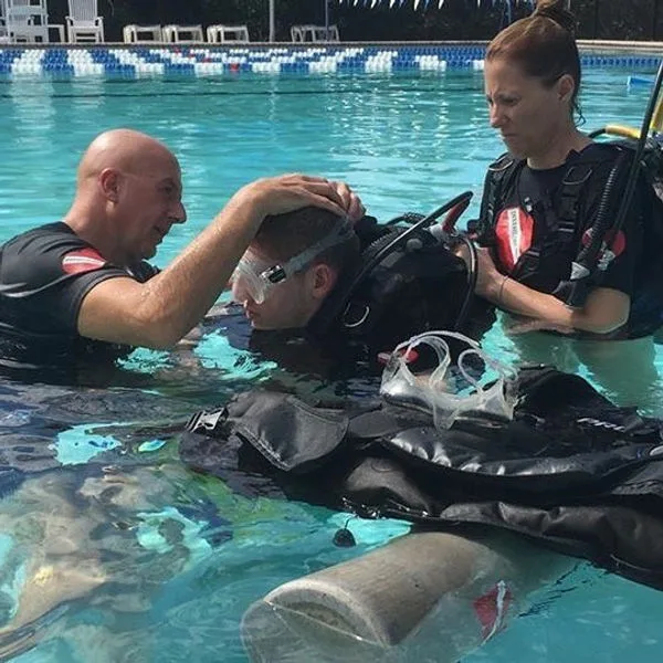 Trois personnes en combinaison de plongée dans une piscine, préparation