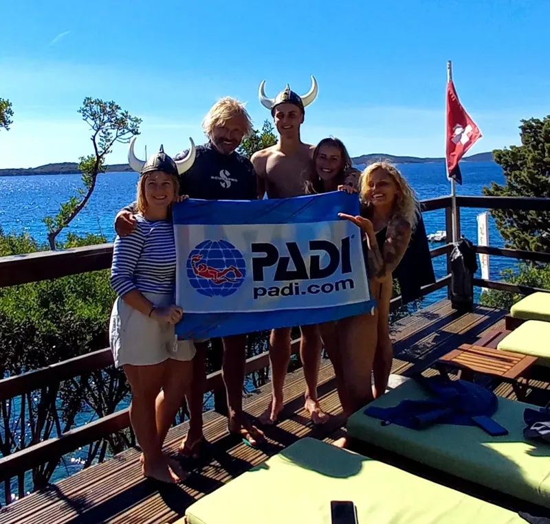 Groupe de personnes souriantes tenant une bannière PADI sur un ponton