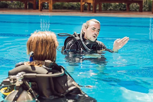 Deux plongeurs en formation dans une piscine, un instructeur explique