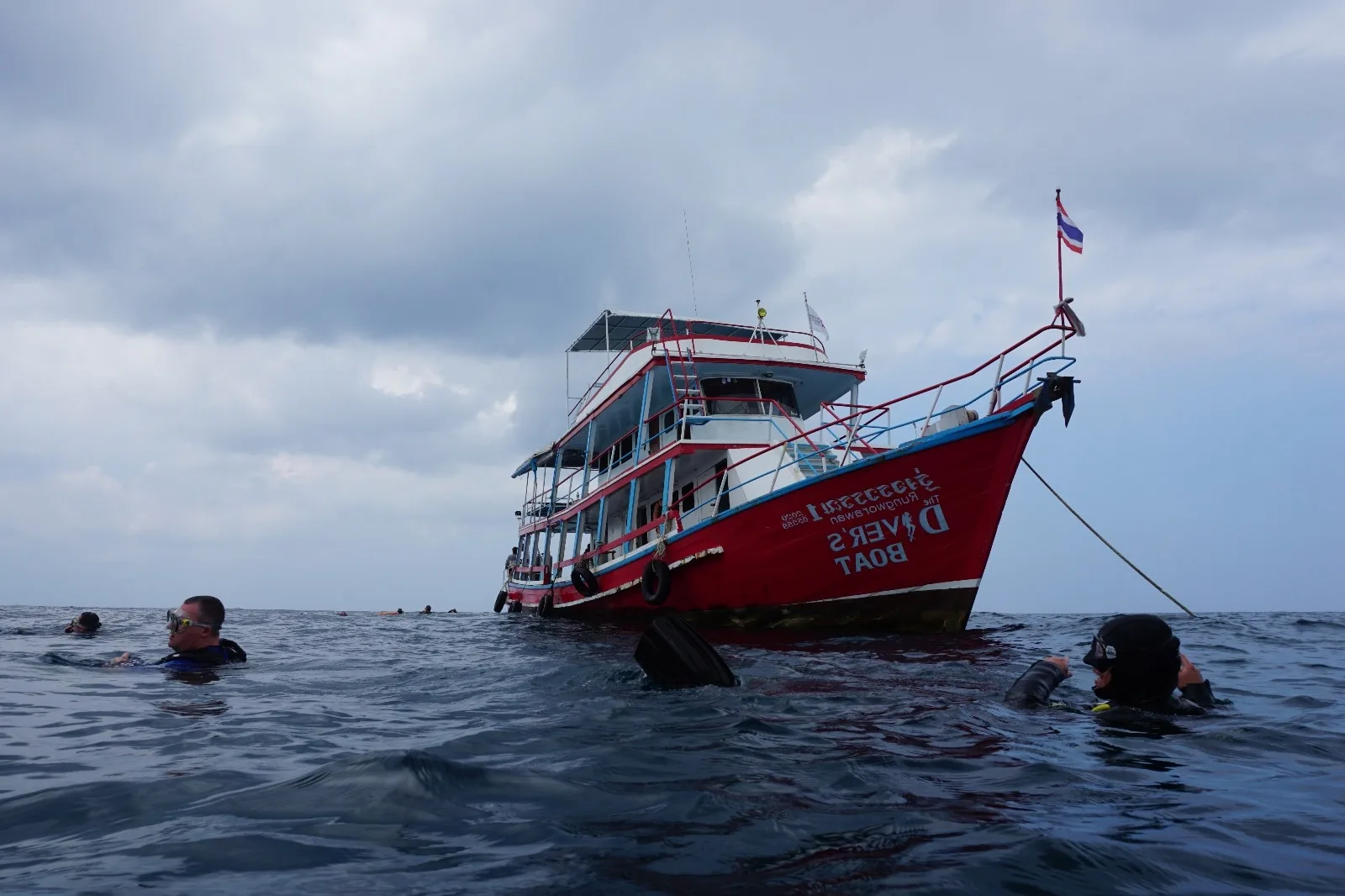 Plongeurs en surface près d'un bateau rouge et bleu sous ciel nuageux