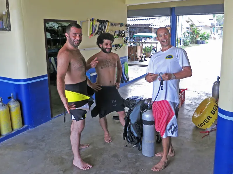 Trois hommes souriants avec équipement de plongée dans un local
