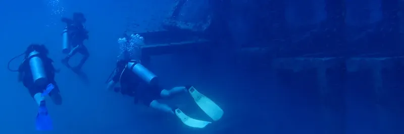 Trois plongeurs explorent une épave sous-marine dans l'eau bleue