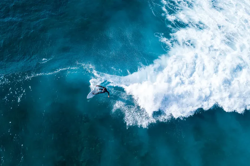 Surfeur sur une vague turquoise, vue aérienne, eau écumante