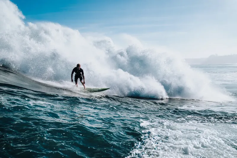 Surfeur sur une vague puissante, eau turquoise et ciel bleu clair