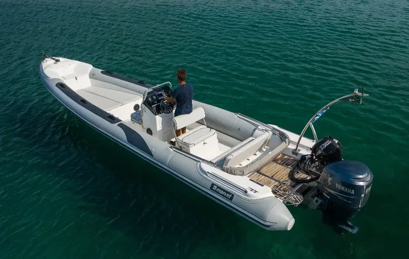 Bateau semi-rigide blanc et gris avec une personne à la barre en mer