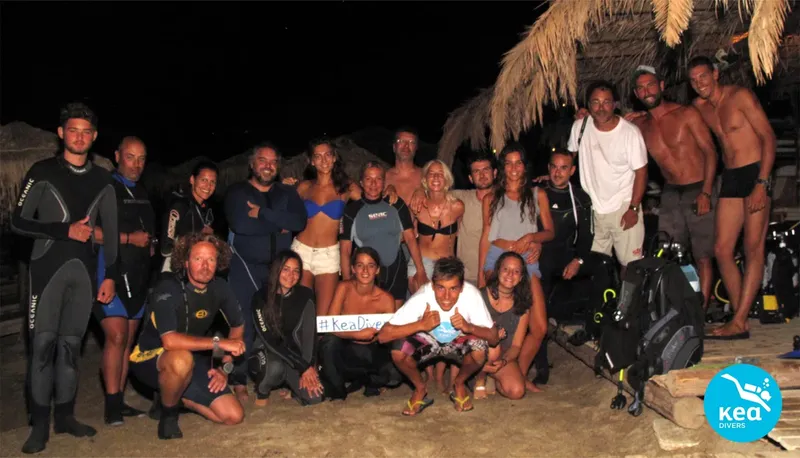 Groupe de personnes souriantes sur une plage, équipement de plongée visible
