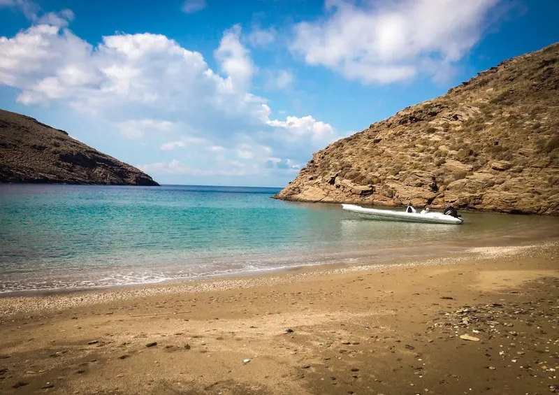 Plage de sable, eau turquoise, bateau amarré dans une crique rocheuse