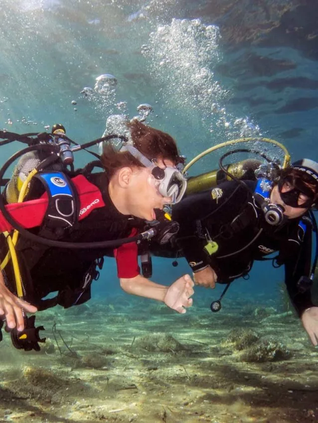 Deux plongeurs en combinaison explorent les fonds marins, bulles remontent