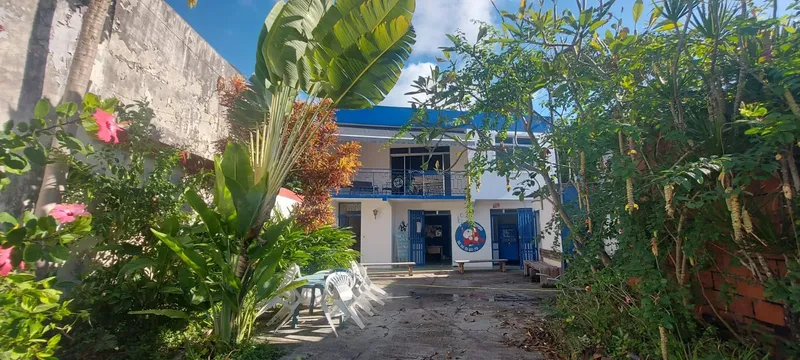 Façade d'un bâtiment avec végétation tropicale et quelques chaises en plastique