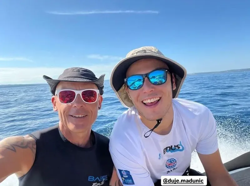 Deux hommes souriants en mer, portant des lunettes de soleil et casquettes